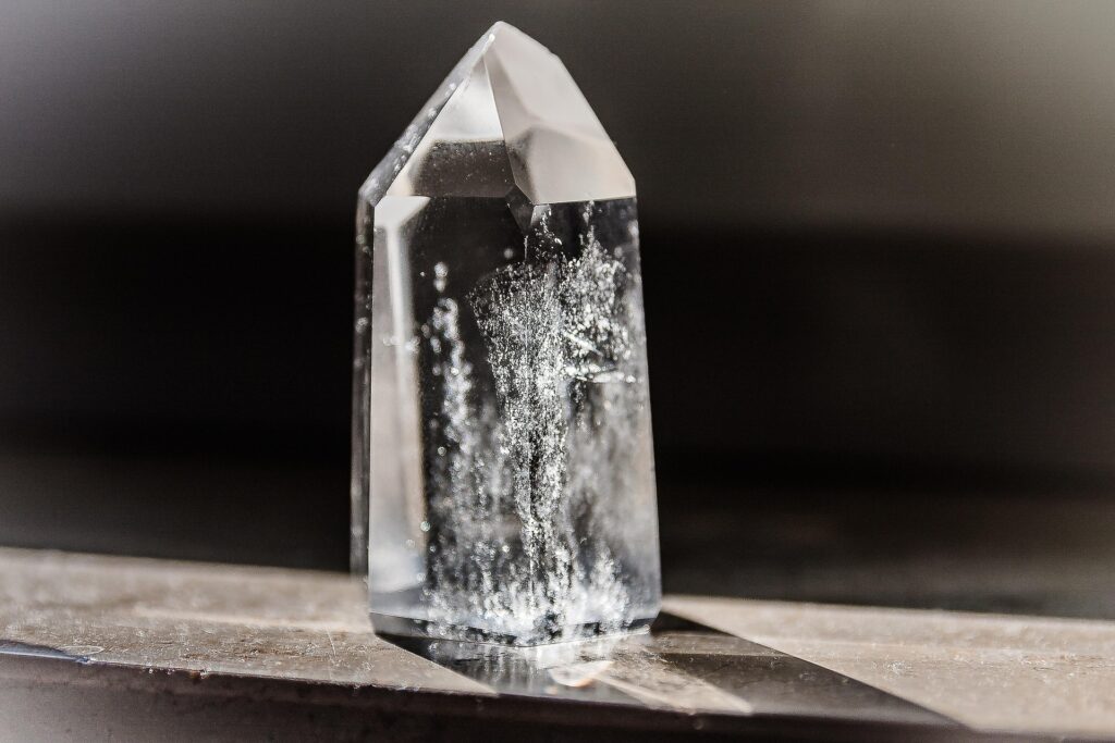Clear quartz point on a grey surface with a black backround.